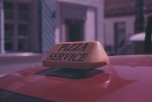 a pizza service sign on the roof of a red car