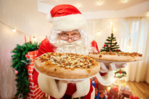 a man in a santa suit holding two pizzas