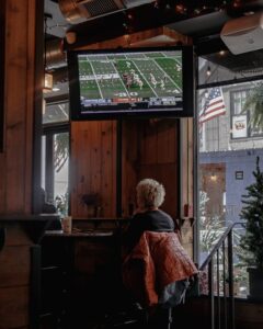 a woman sitting at a bar watching a football game on the tv