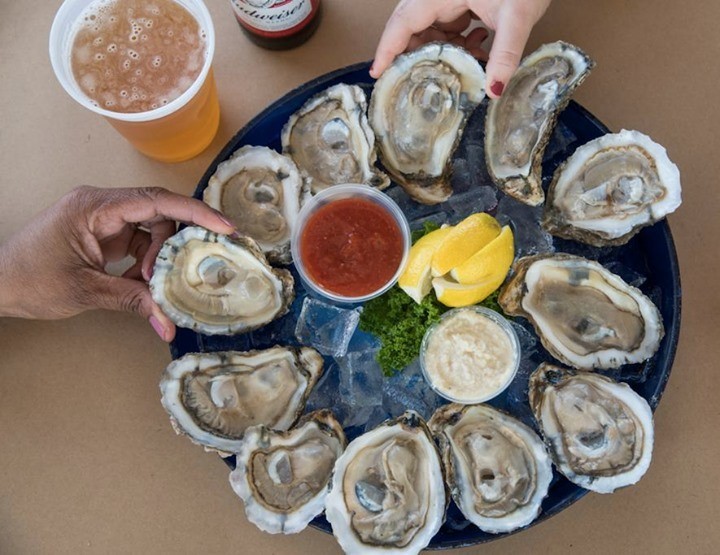 close up of oysters on platter with hands holding two of them and beers