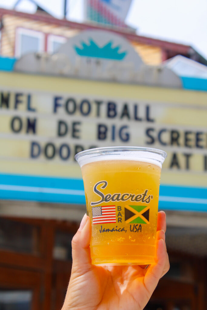 a person holding a cup of beer in front of a sign