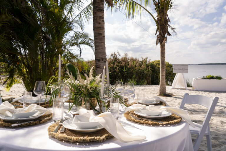 a table set up for a formal dinner on the beach