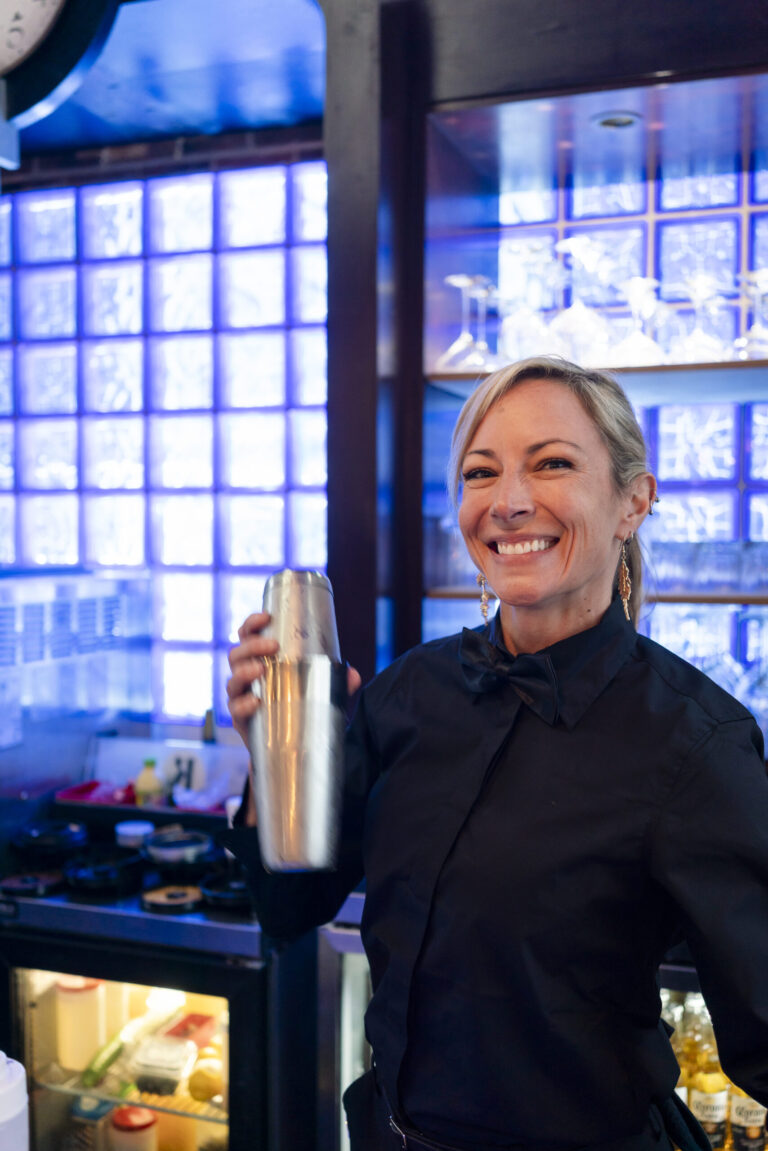 a woman standing in front of a counter holding a shaker