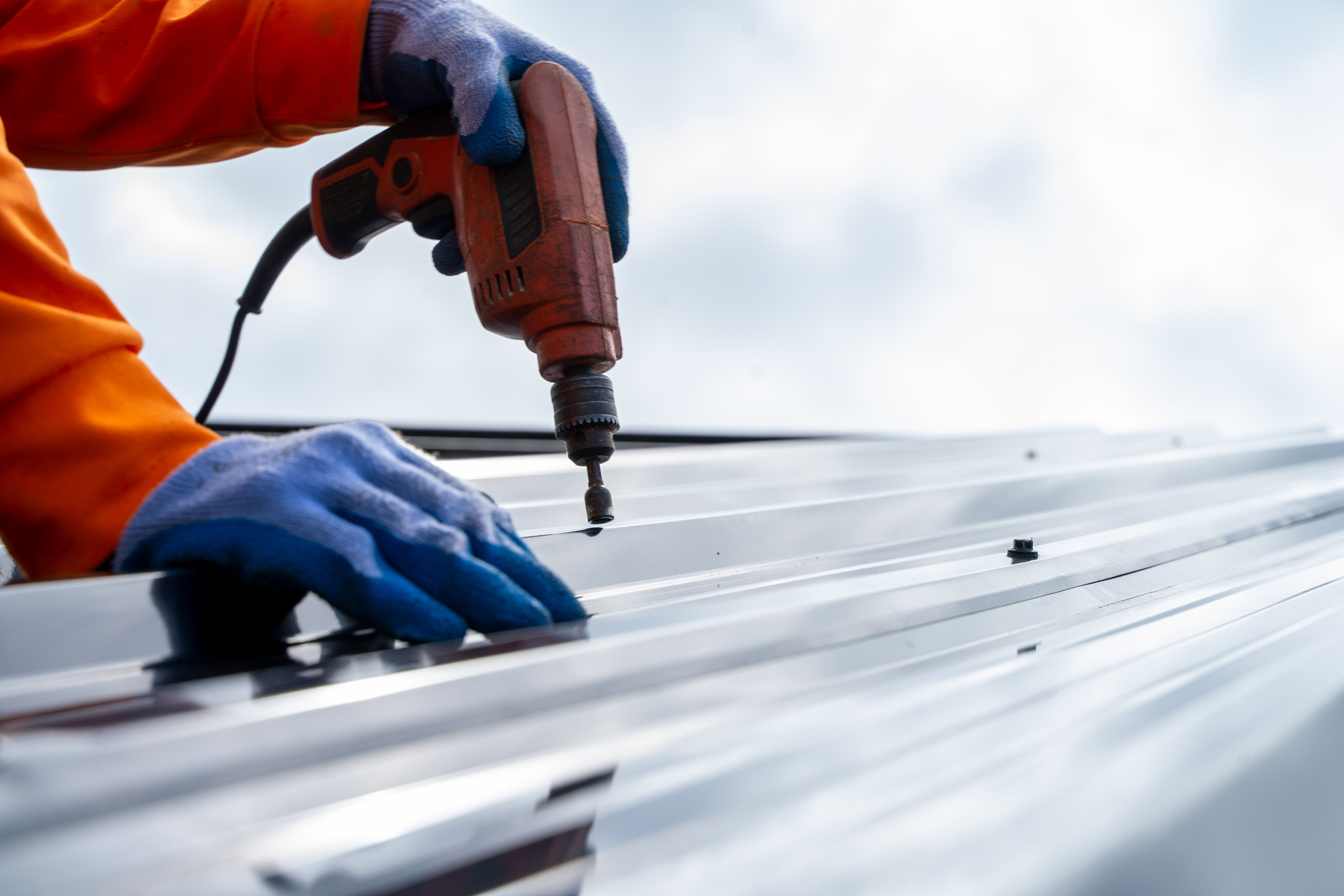 a man in orange jacket and blue gloves working on a metal roof