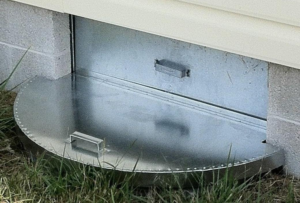 a metal crawl space access door sitting in the grass next to a building