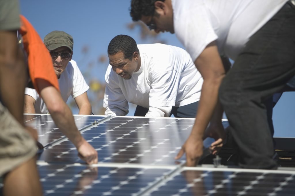 Group of multiethnic engineers placing solar panel on rooftop