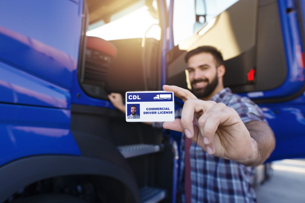 Portrait of middle aged bearded truck driver standing by his truck and showing his commercial driver license. Focus on CDL license.