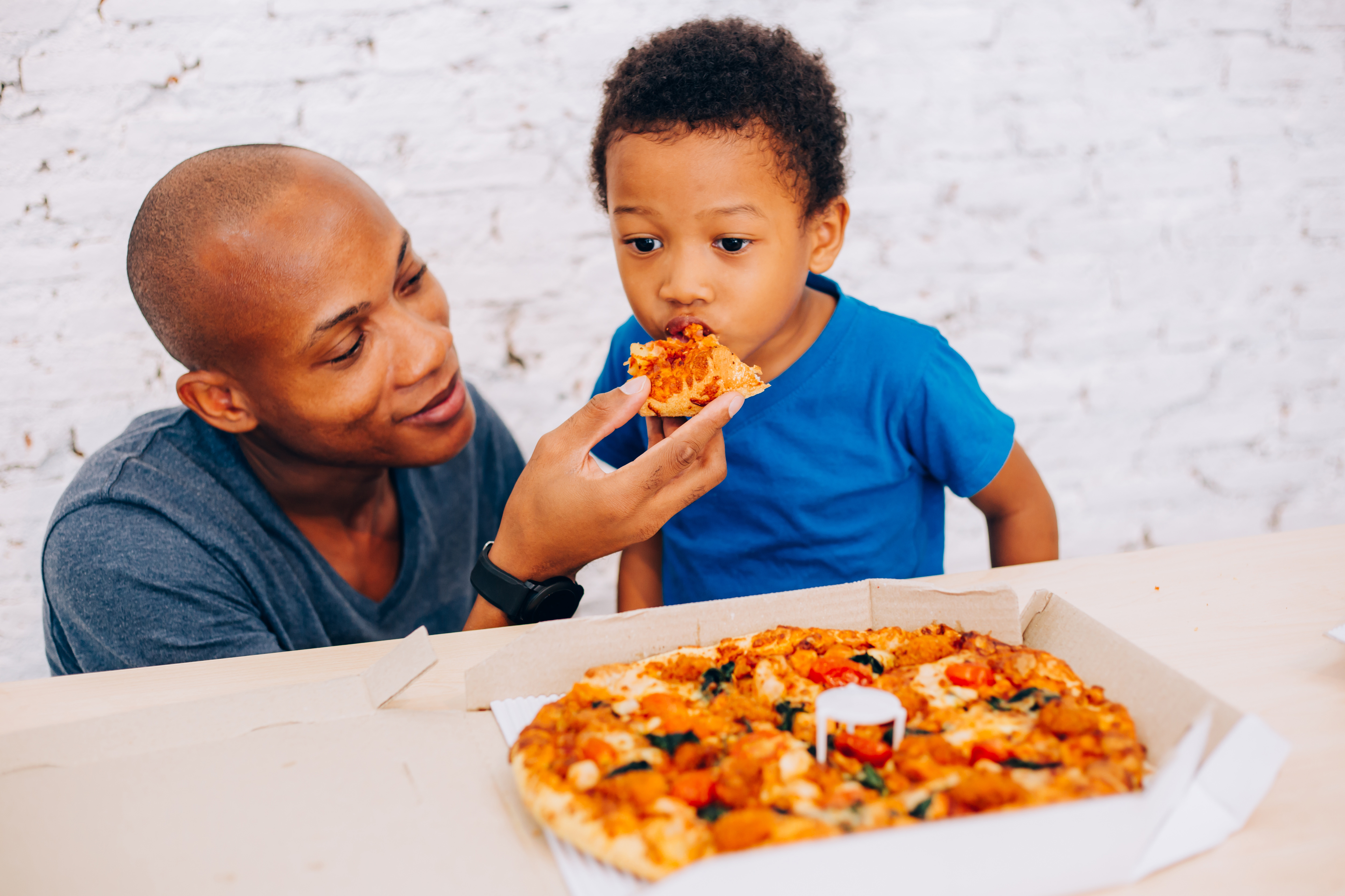father feeding pizza to son