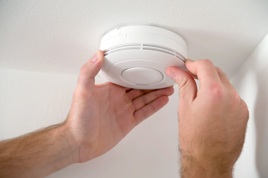 a man adjusting a smoke detector on a wall