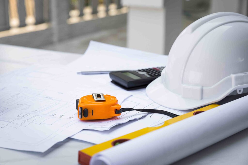 contractors helmet, measuring tape, plans, calculator on table