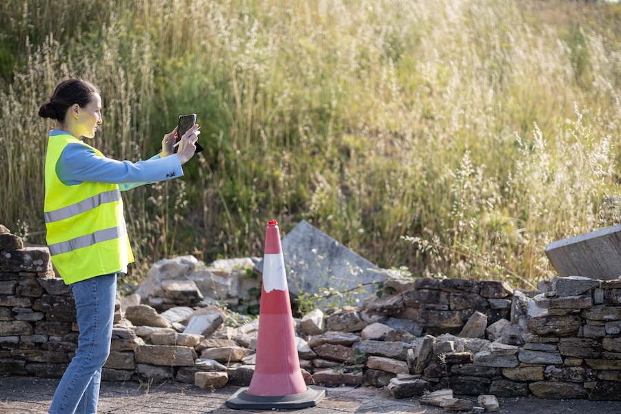 person in safety vest taking picture behind a cone