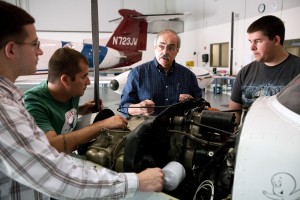 four men standing around plane engine being worked on