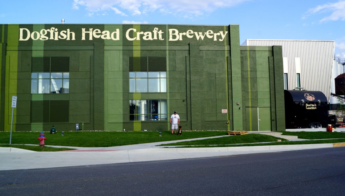 green brewing building with man and dog standing out front