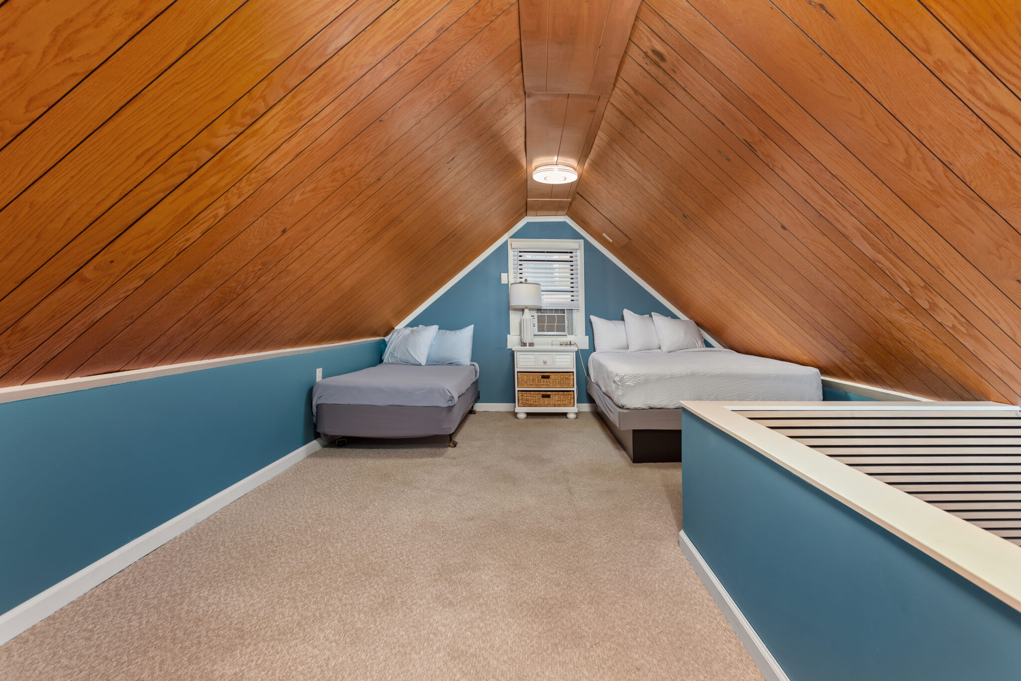 A room with a sloping wood ceiling, blue walls, and two beds.