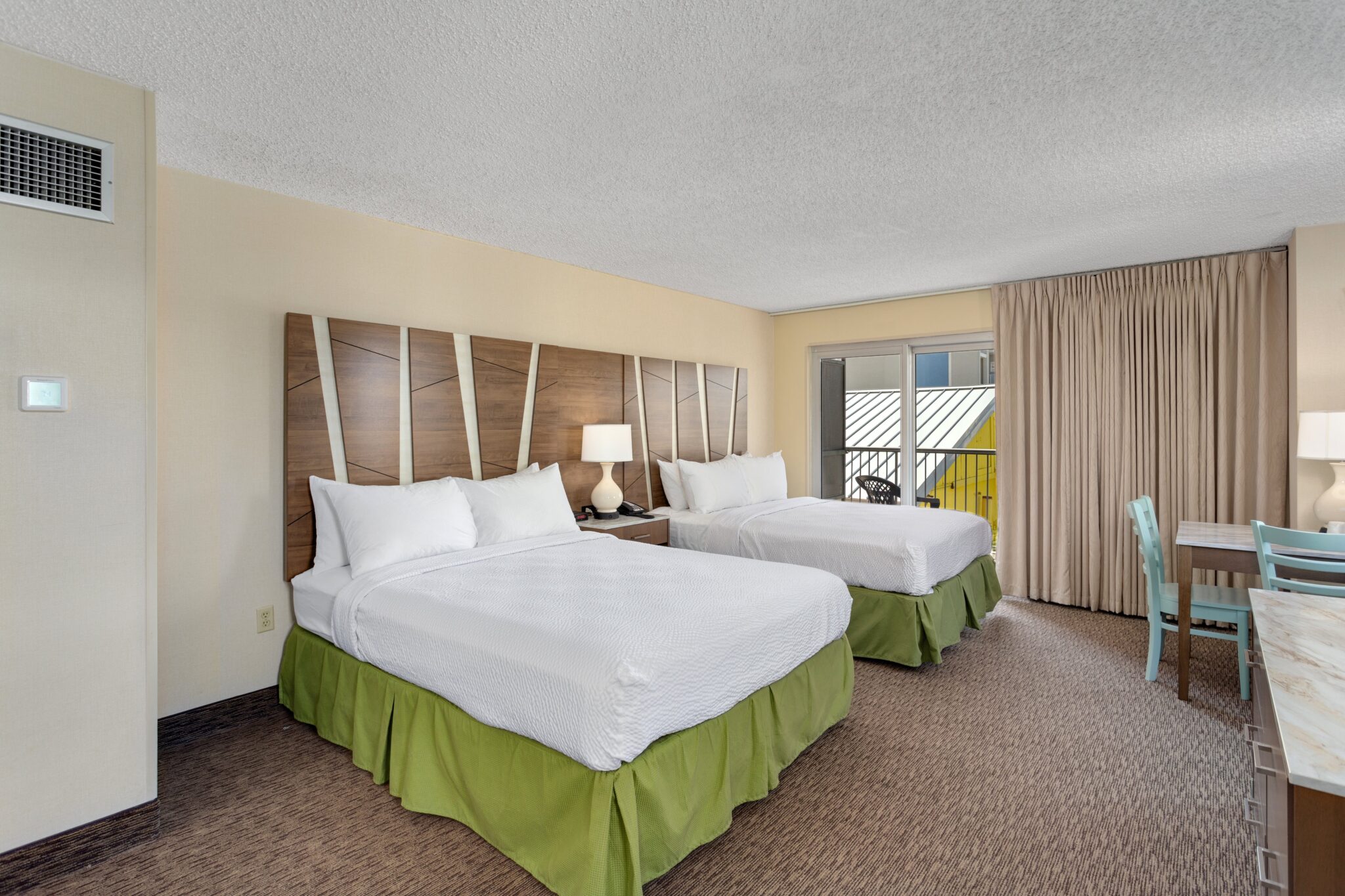 A hotel room with two beds, a desk, and a balcony