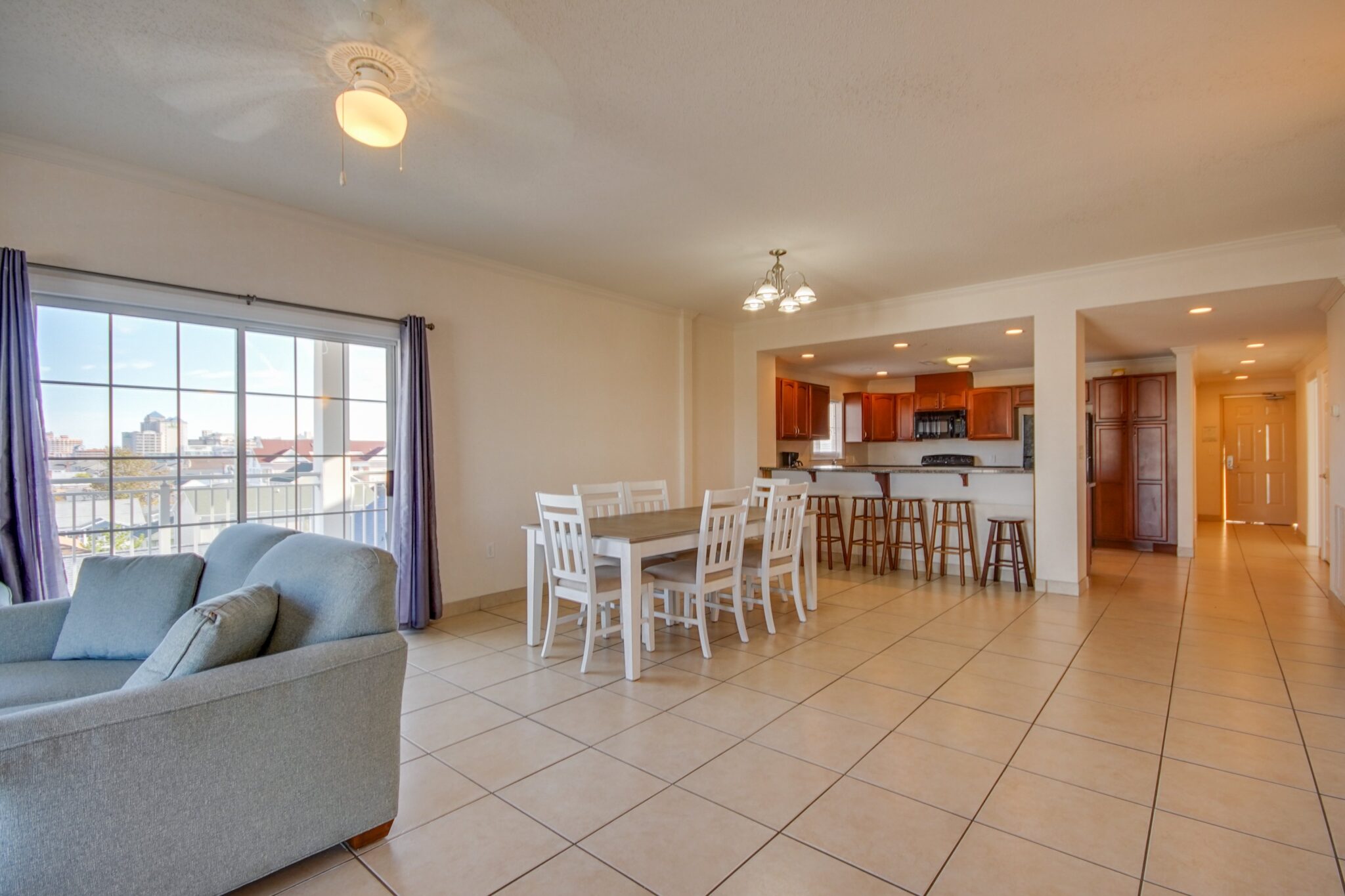 A wide view of a living area with a sofa, dining table, kitchenette, and large window.