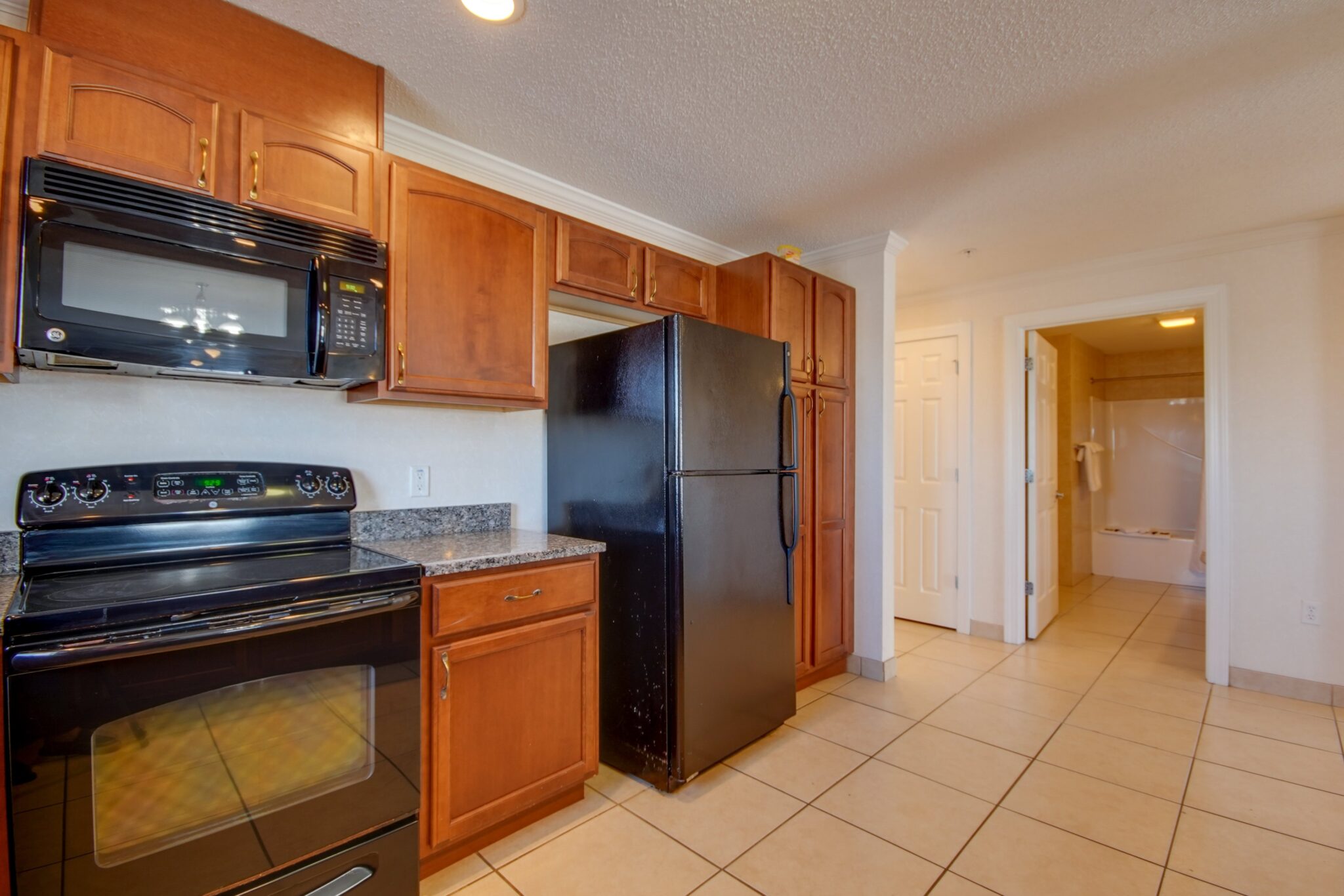 A kitchen with black appliances, wooden cabinets, and a tiled floor.