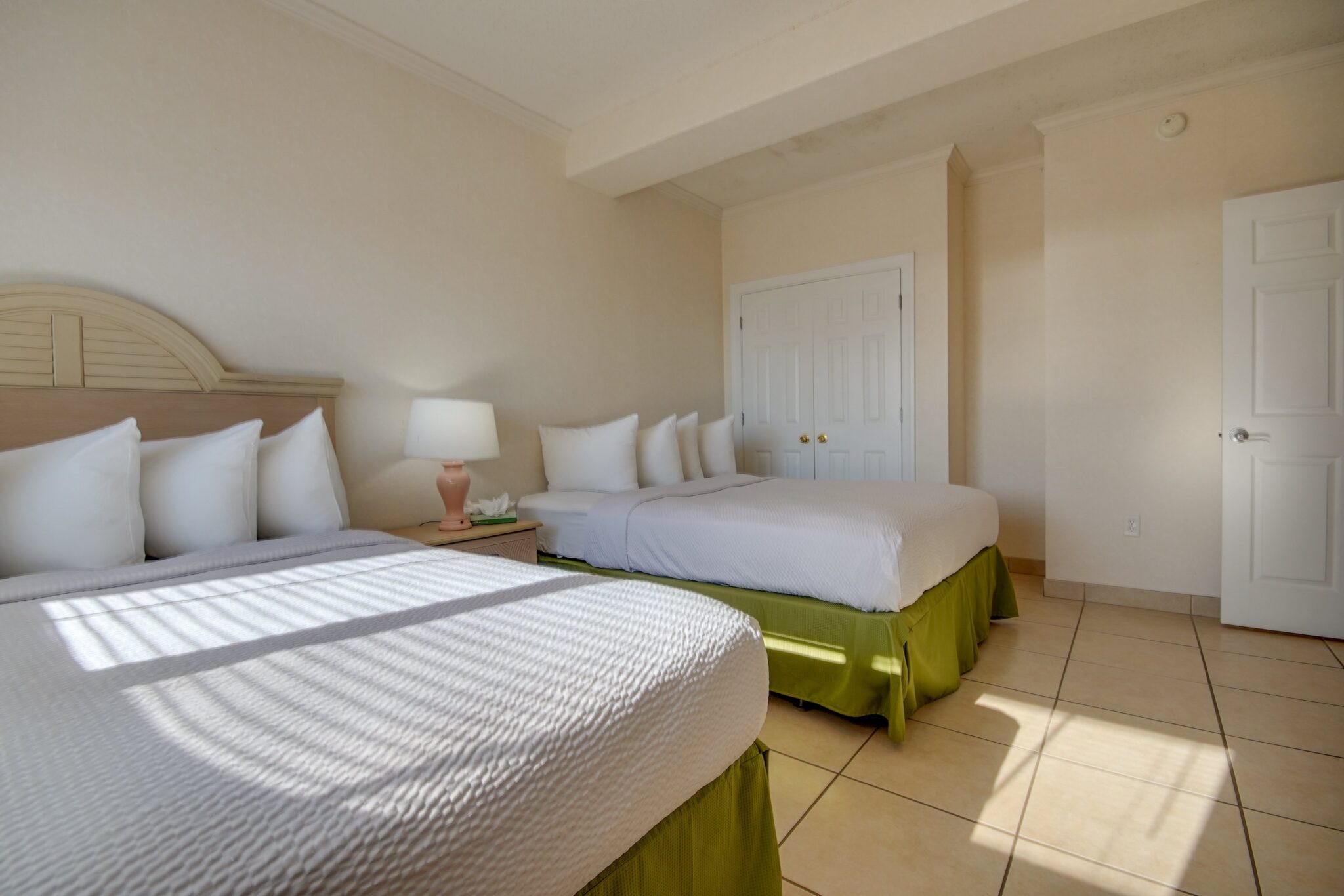 A hotel room with two beds, white bedding, and green skirts.