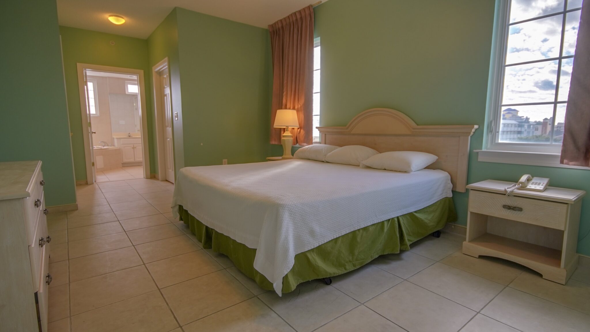 A wide view of a hotel room with a bed, nightstand, and window