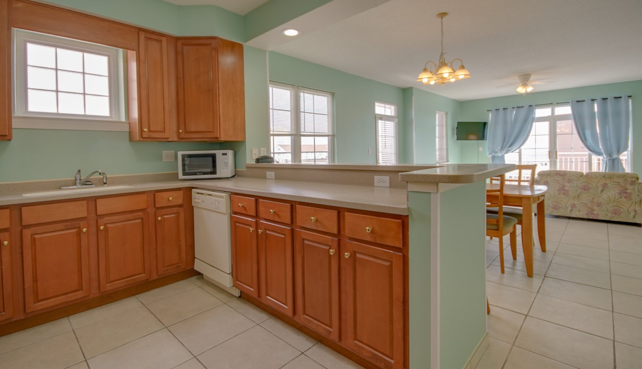 A wide view of a kitchen with wooden cabinets, a microwave, and a dining area.