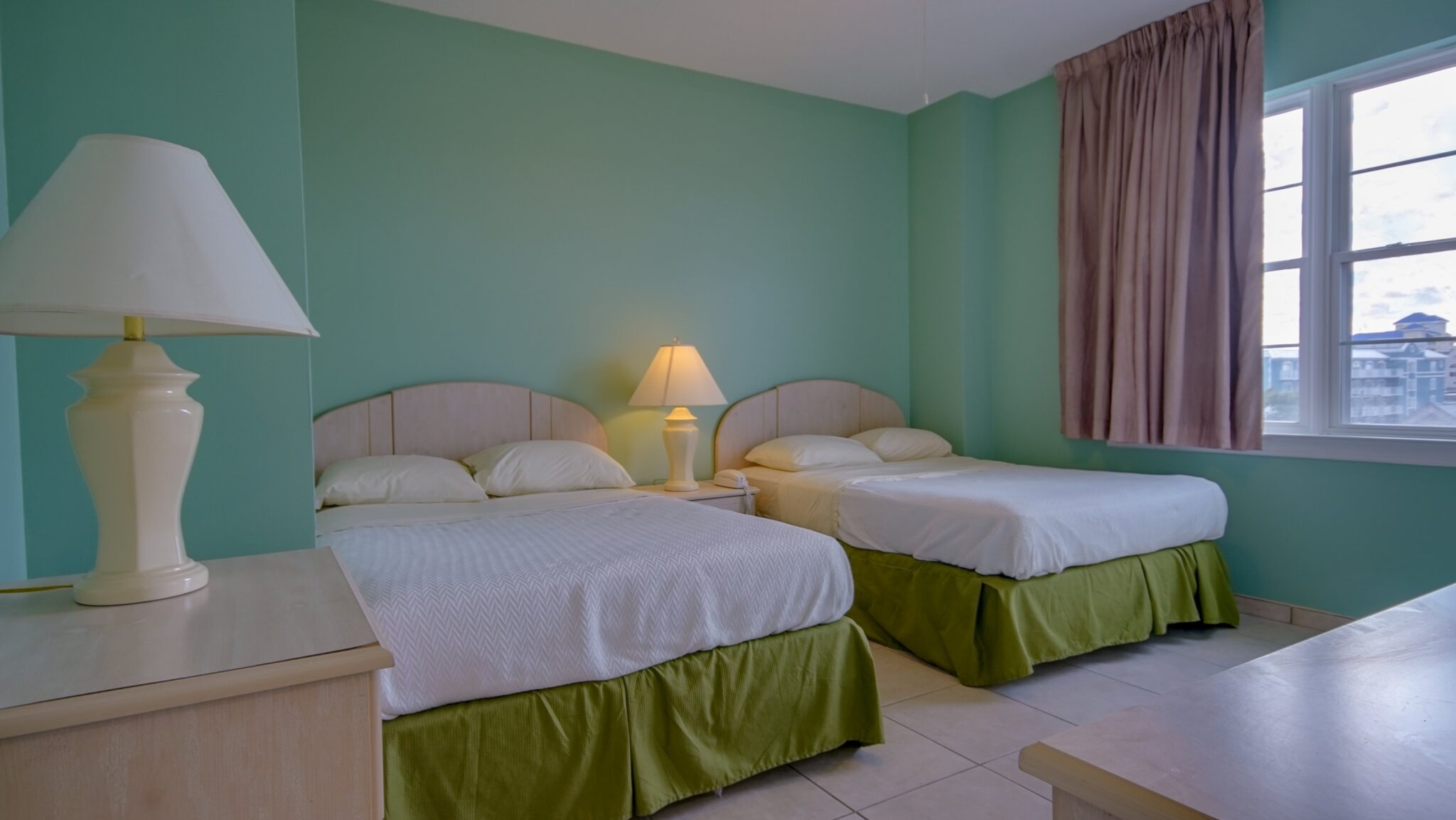 A hotel room with two twin beds, lamps, and a window.