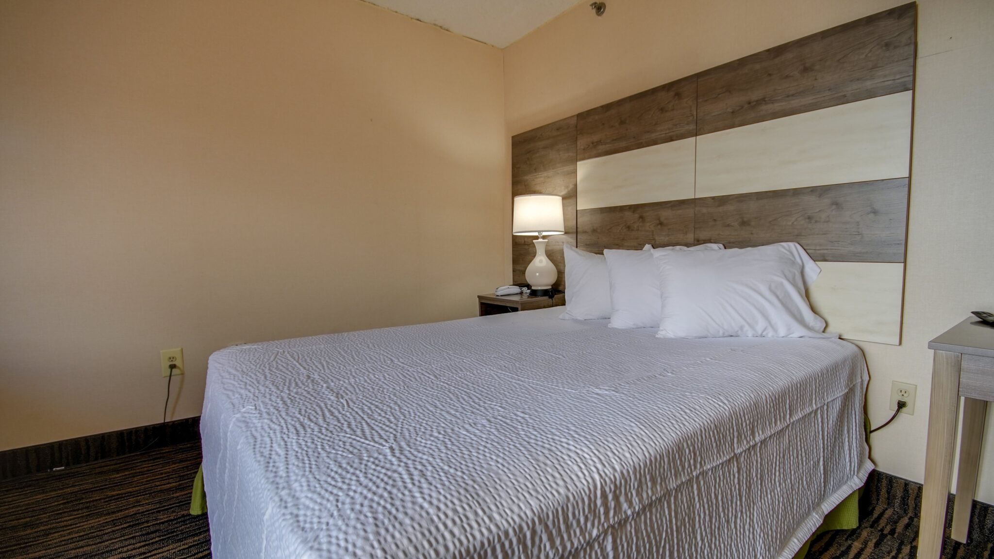 A hotel room with a large bed, nightstand, and lamp.