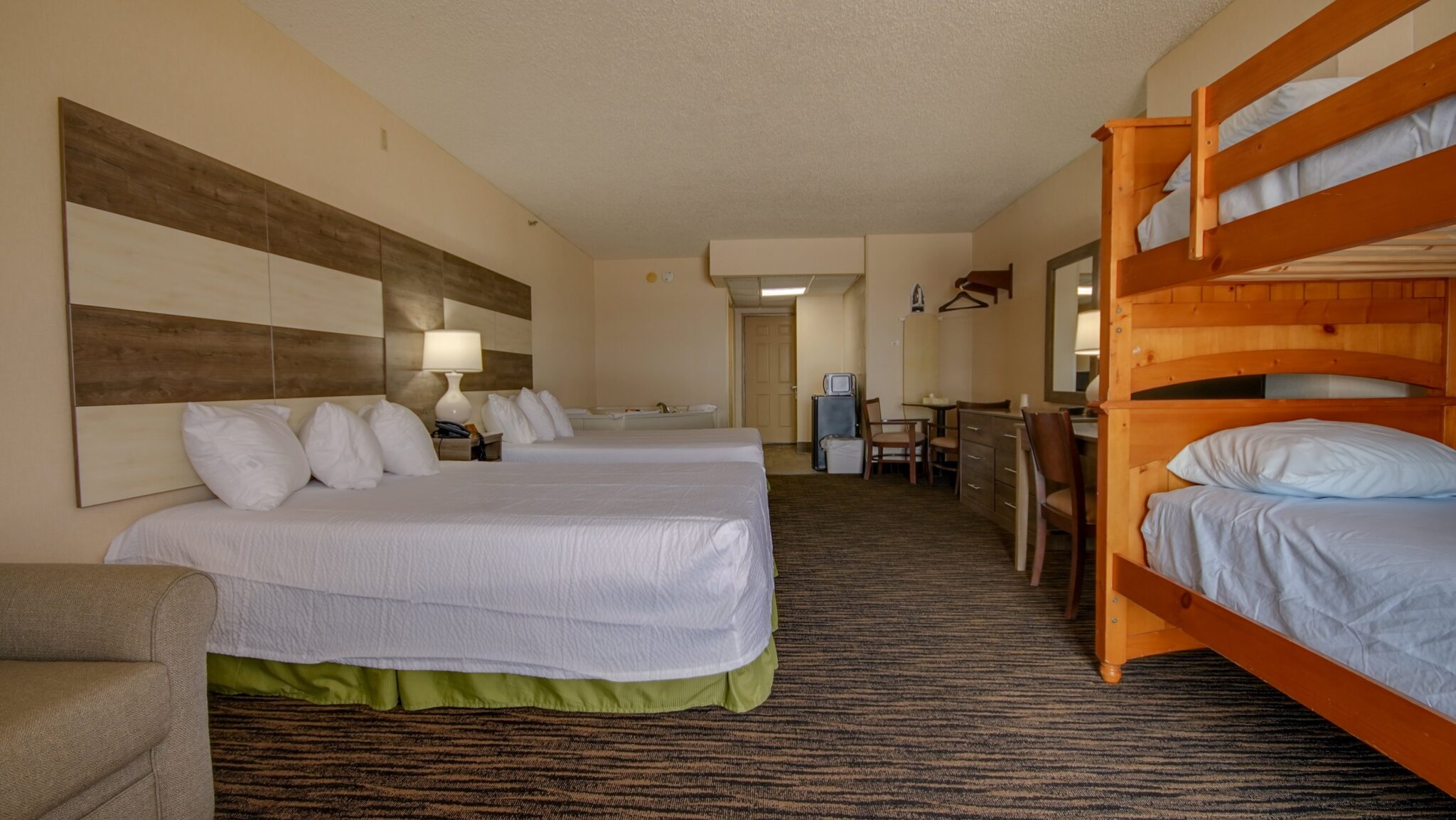A hotel room with two queen beds, a bunk bed, a desk, and a small refrigerator.