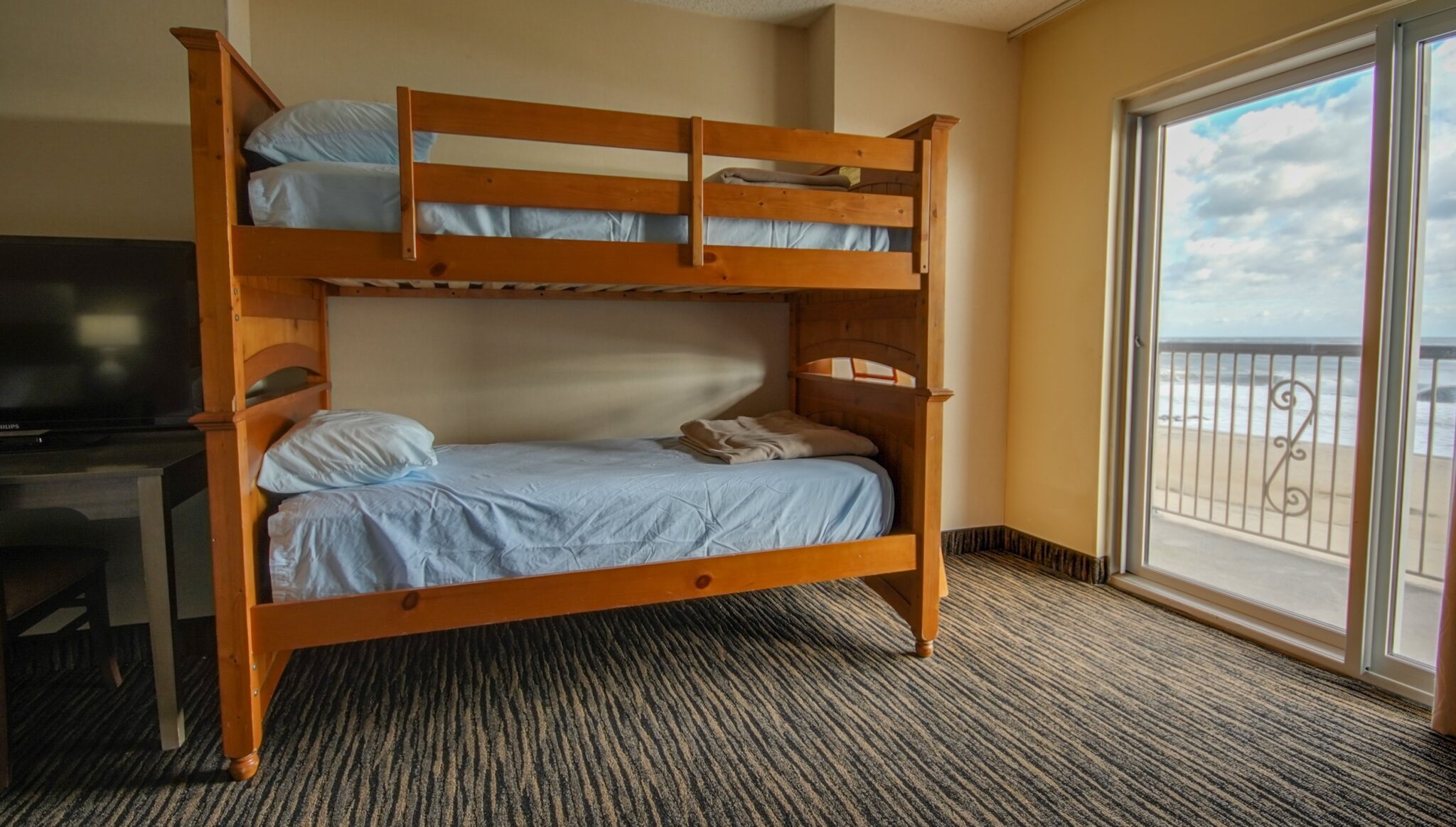 A room with bunk beds, a TV, and a sliding glass door leading to a balcony with an ocean view.