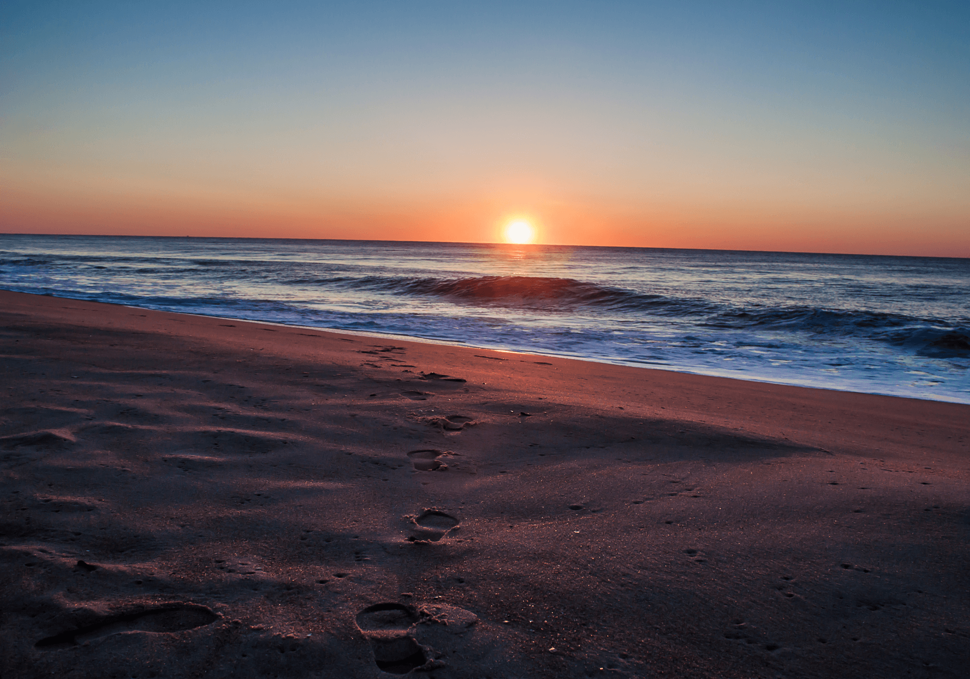 a beach at sunset with the sun setting over the ocean