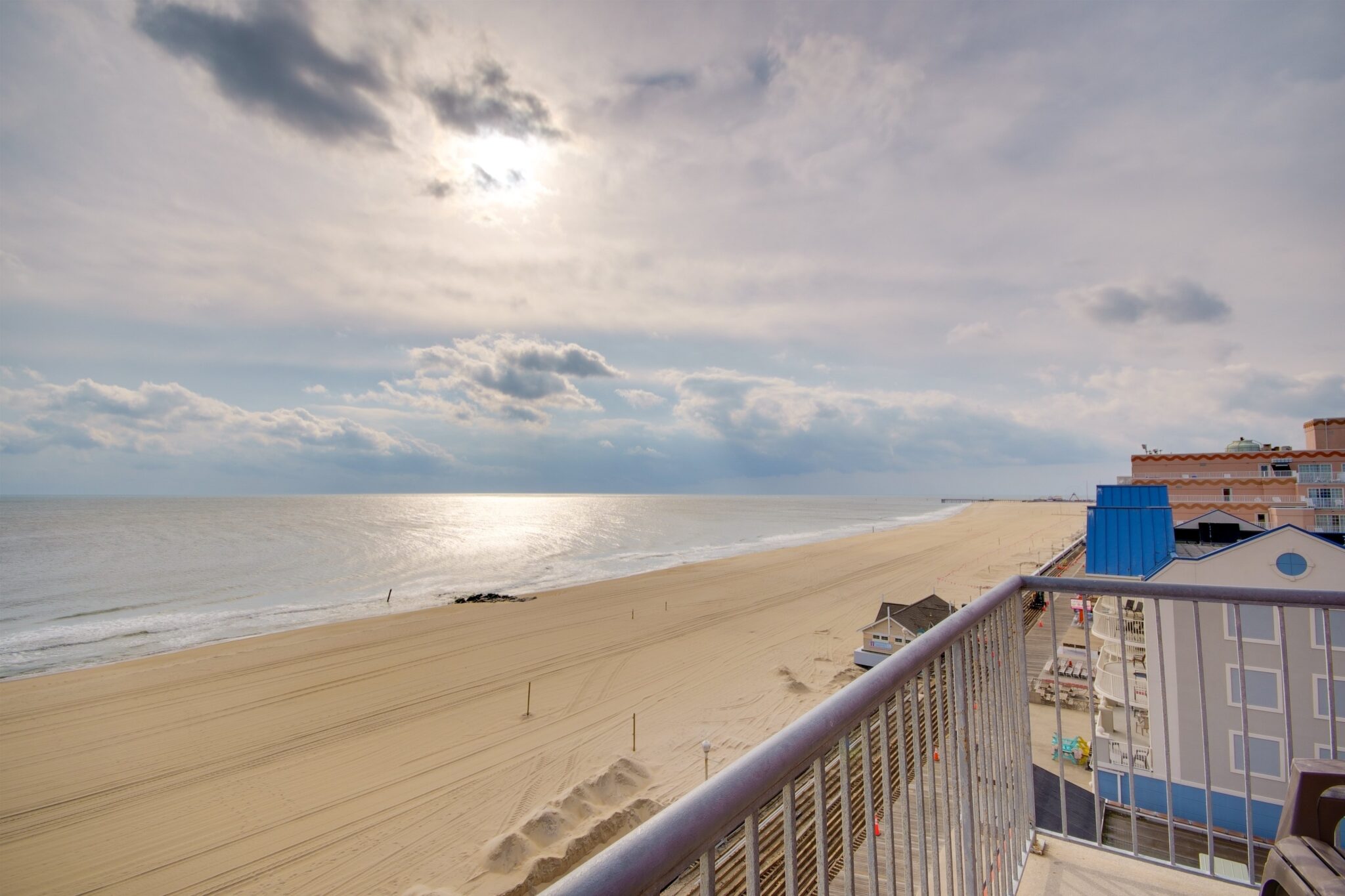 A beachfront view from a balcony with a cloudy sky and ocean in the background.