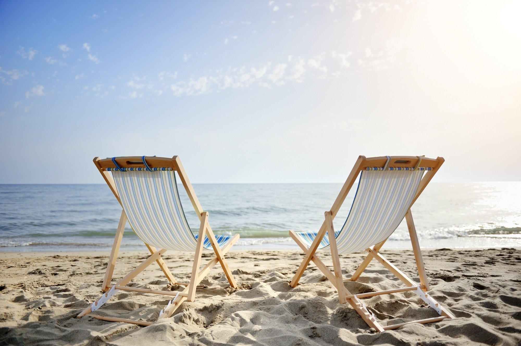 Two beach chairs on a sandy beach overlooking the ocean.