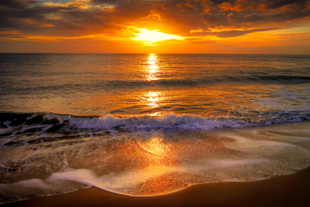 a sunset over the ocean with waves coming in