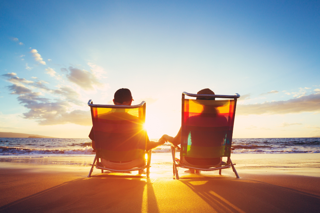 two people sitting in lawn chairs facing the ocean at sunset