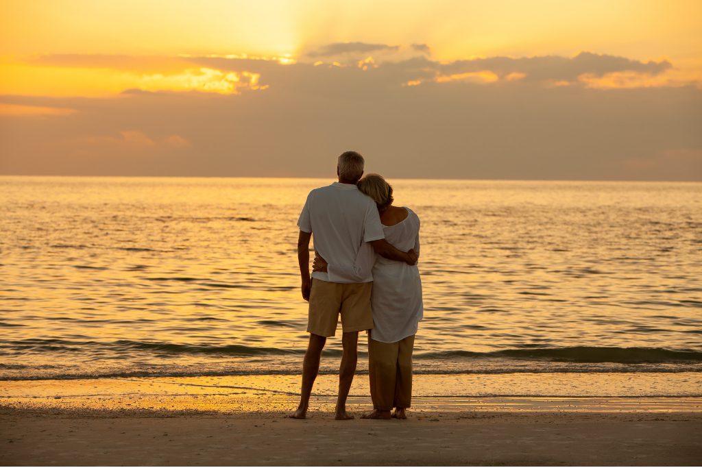 A couple stands on the beach at sunset, looking out at the ocean.