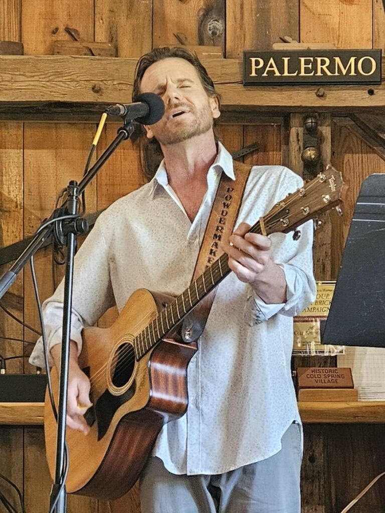 A man singing into a microphone with this acoustic guitar