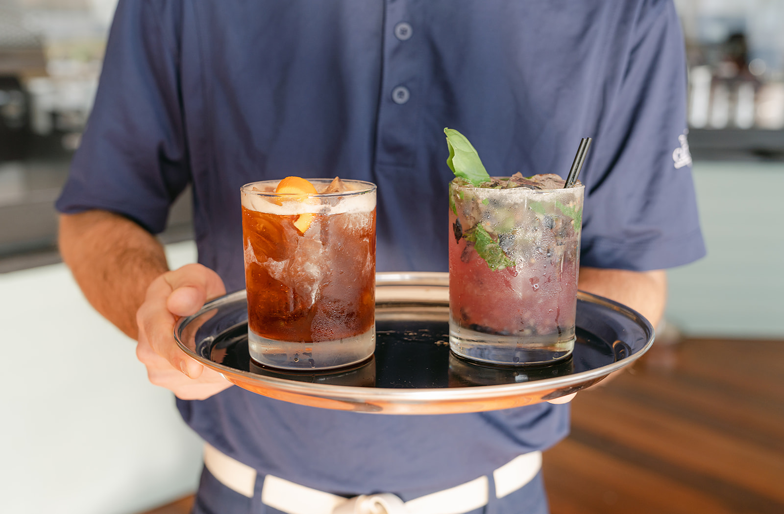 a man holding a tray with two drinks on it