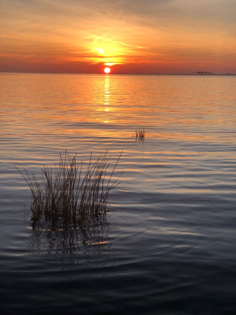 the sun setting over the water with a small island in the middle