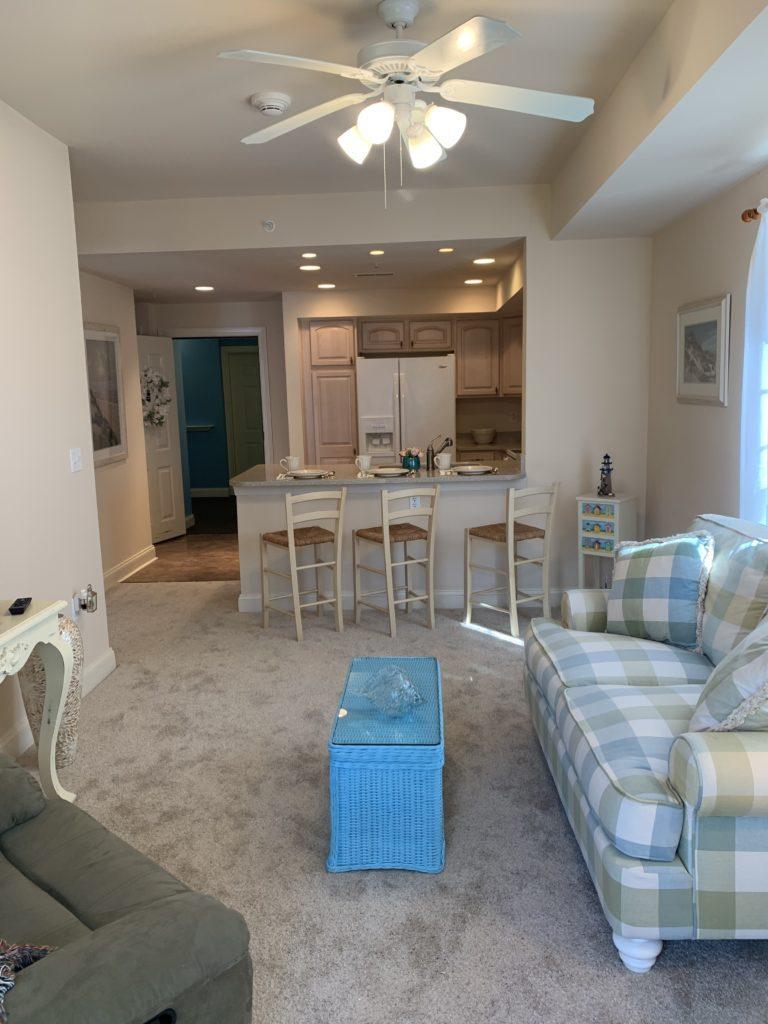 unit living area with love seat, recliner, ceiling fan, and full kitchen in background
