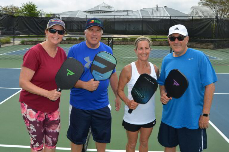 four people standing on a tennis court holding racquets