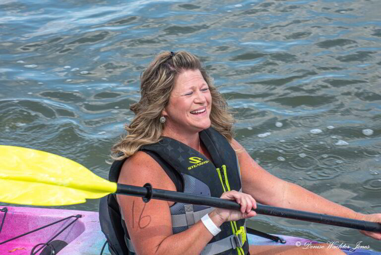 a woman in a kayak smiles as she sits on the water
