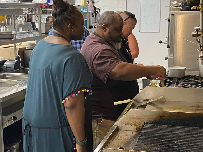 three people in a kitchen preparing food on a grill