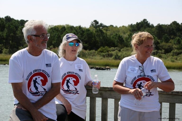 three people sitting on a wooden fence by the water