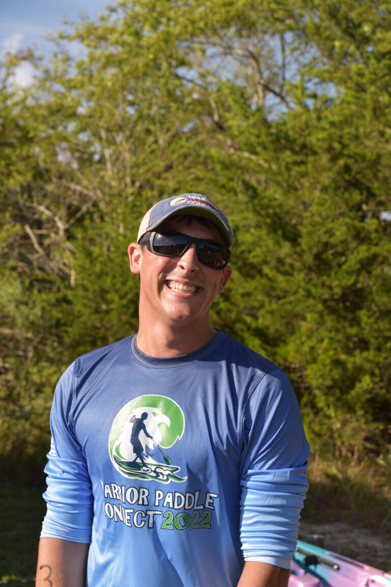 a man in a blue shirt and sunglasses standing next to a pink surfboard