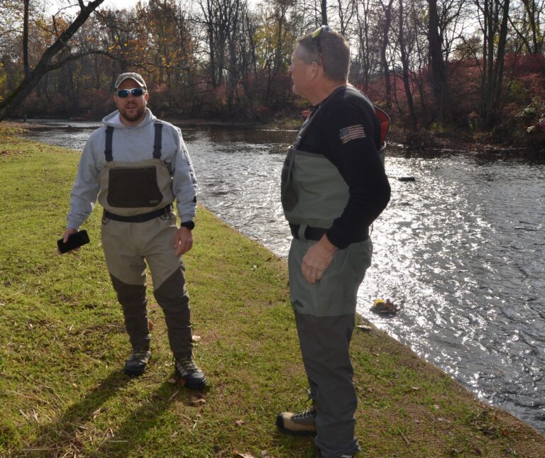 two men standing next to each other near a river