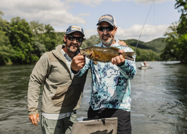 a couple of men standing on top of a river holding a fish