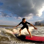 girl balancing on red surfboard as she takes the wave into shore