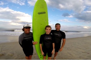 three people pose with green surfboard on the beach