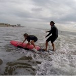 Instructor helping girl stand up on surfboard