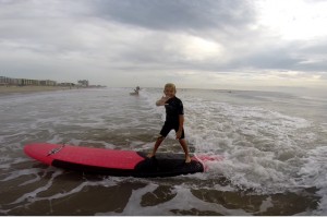little boy waving to camera as he surfs