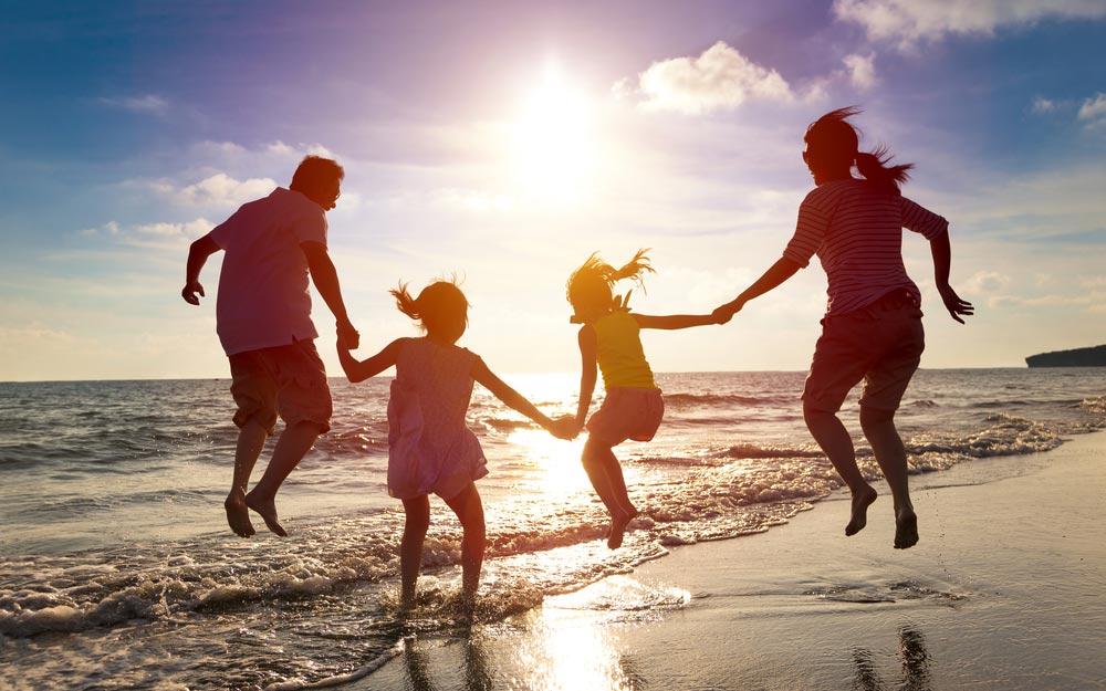 family jumping at edge of beach shoreline at sunset